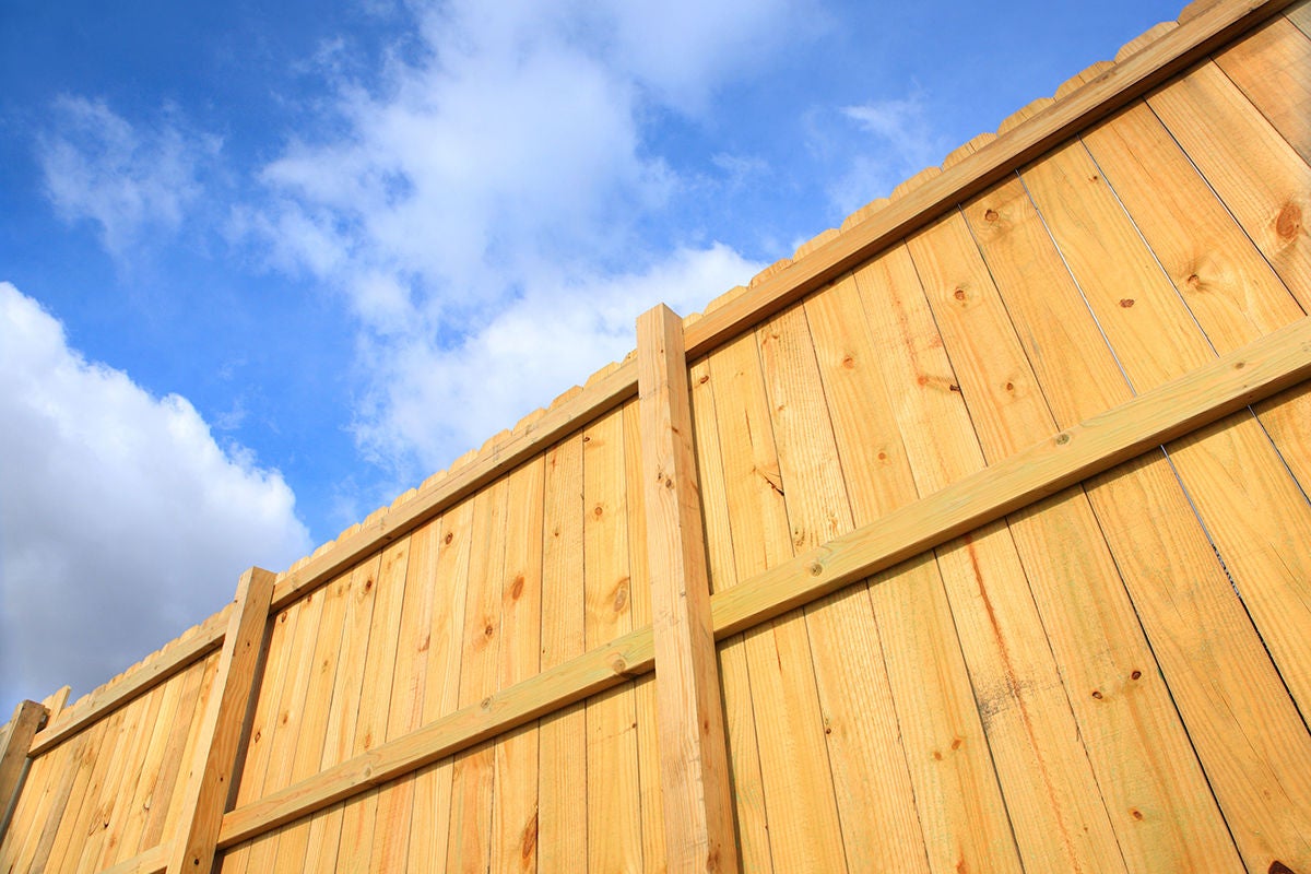 a wooden fence cuts diagonally across the screen with a blue sky and white puffy clouds