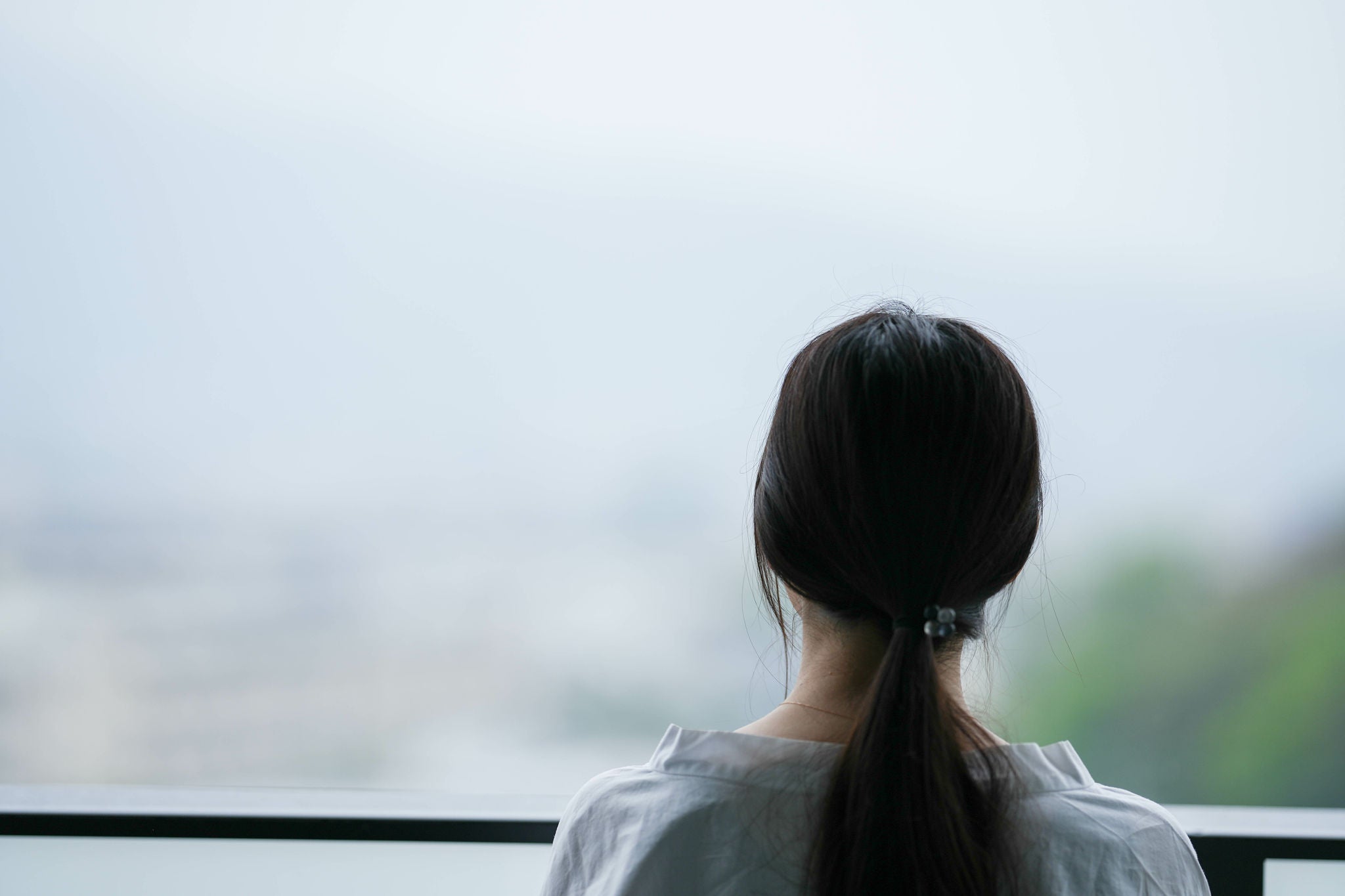 A woman's back is turned to the camera. She is looking out into the distance while standing on a balcony.