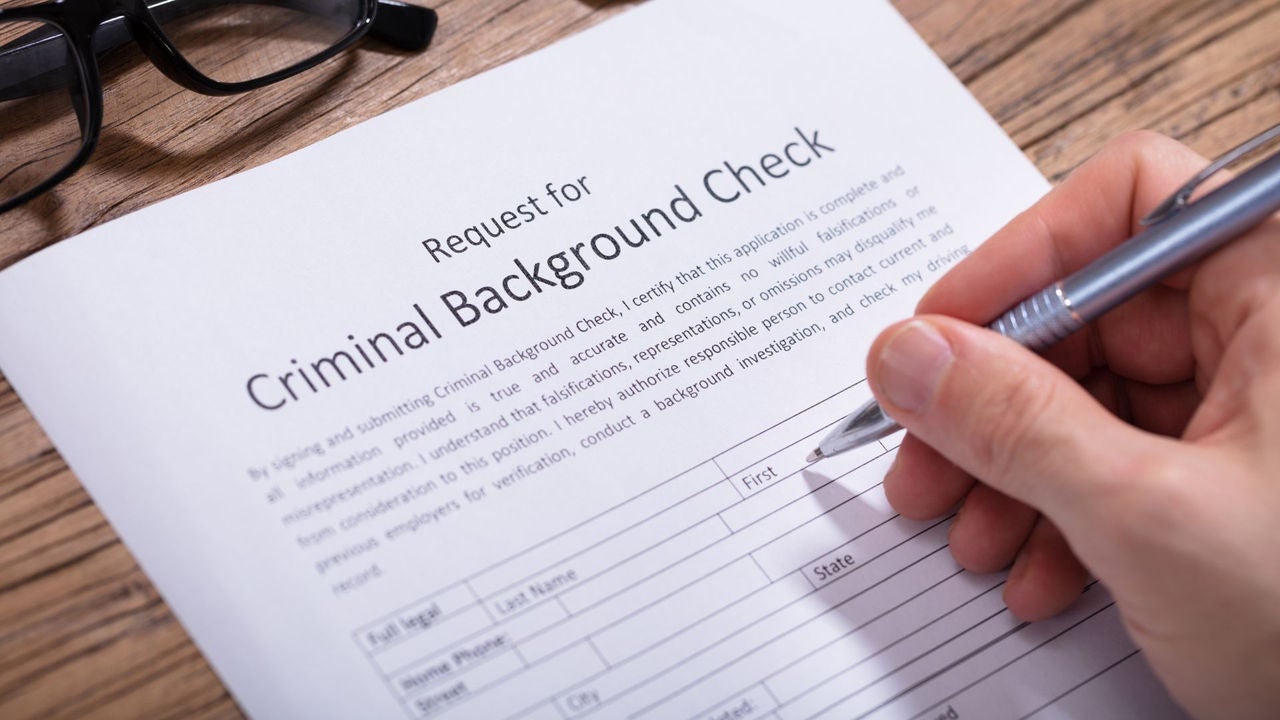 A hand with a pen filling out a Request for Criminal Background Check form