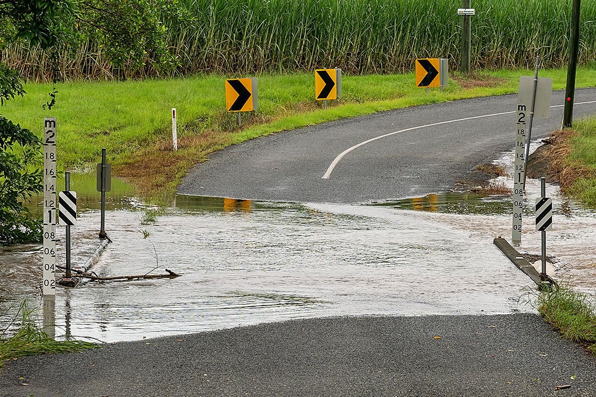 A flooded bridge is in the middle of a roadway. There are water markers either side of the bridge that show the water level is 0.1m